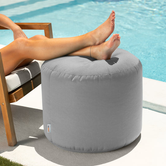 Person relaxing with feet on a gray ottoman by a pool