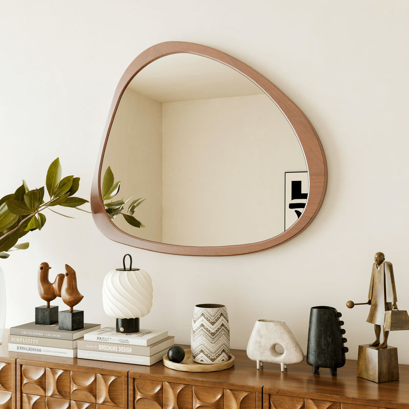 Asymmetrical wood wall mirror above a carved wood sideboard with plants and vases
