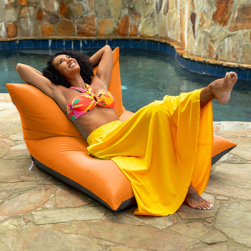Woman relaxing and kicking her feet up on the Finster Outdoor Bean Bag Lounge Chair in Tangerine