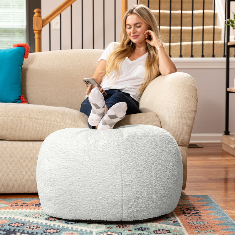 Woman sitting on a beige armchair with a white ottoman in a living room.