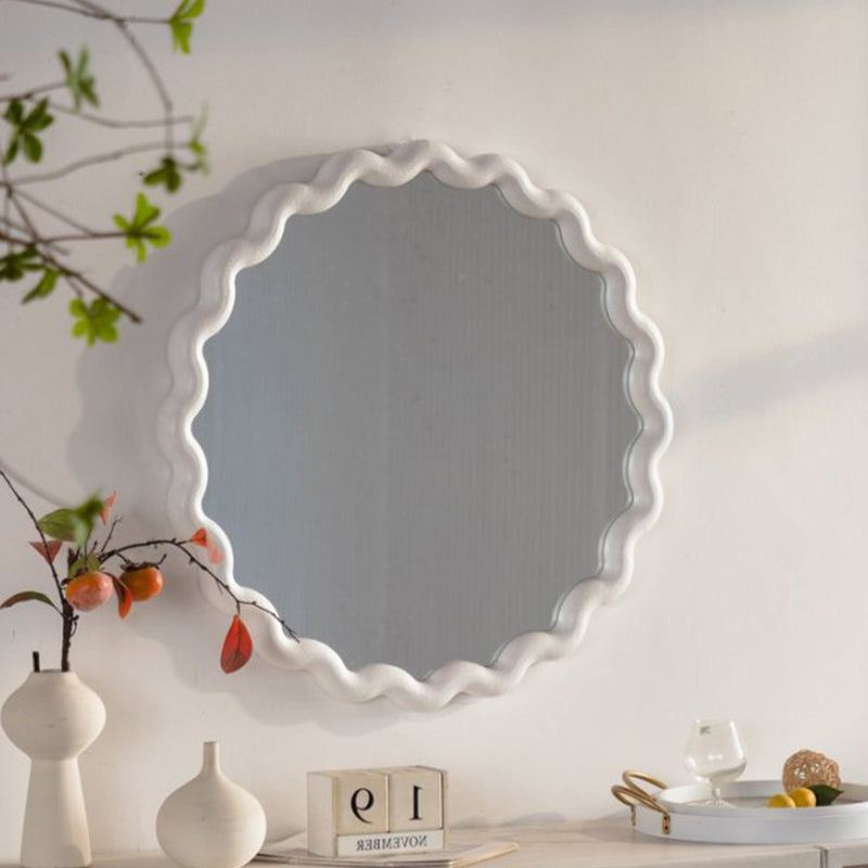 White scalloped round wall mirror above a console with vases