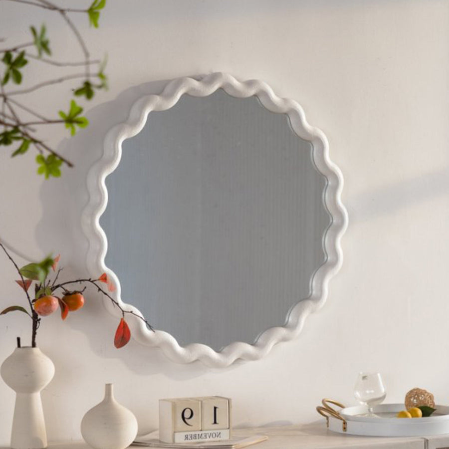 White scalloped round wall mirror above a console with vases