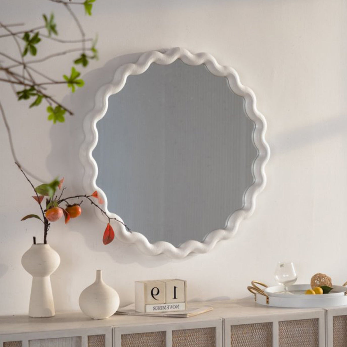 White scalloped round wall mirror above a white sideboard with decor