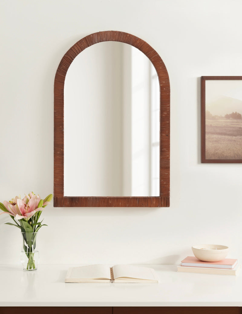 Brown rattan arch mirror above a vanity with flowers