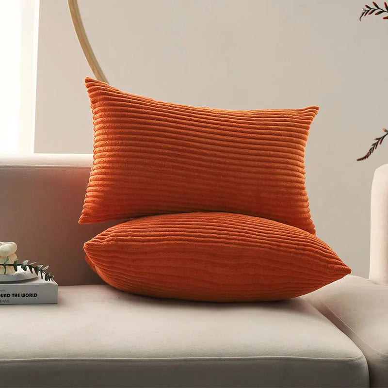 Two orange corduroy lumbar pillows stacked on a sofa