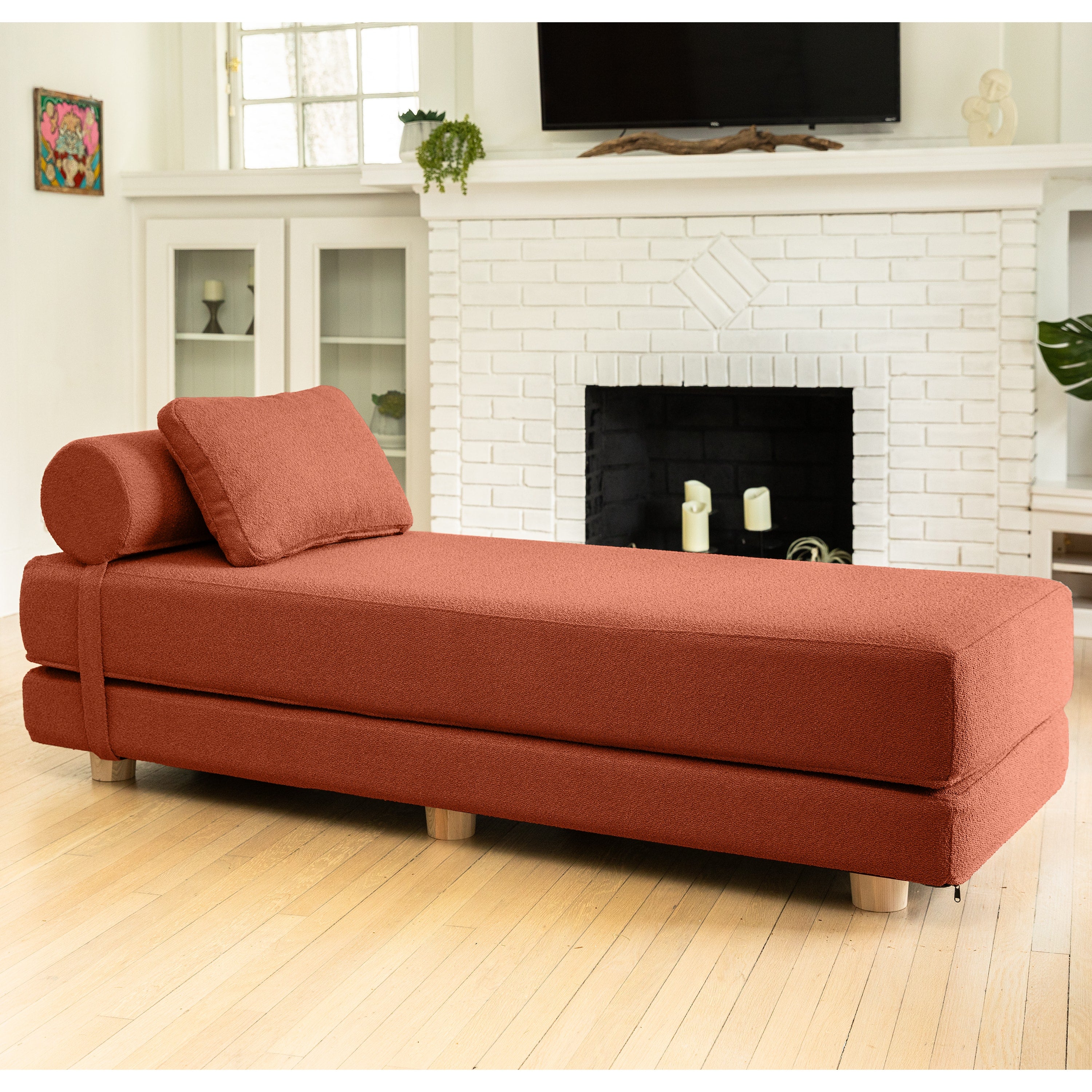 Red sofa bed in a living room with a fireplace and TV.