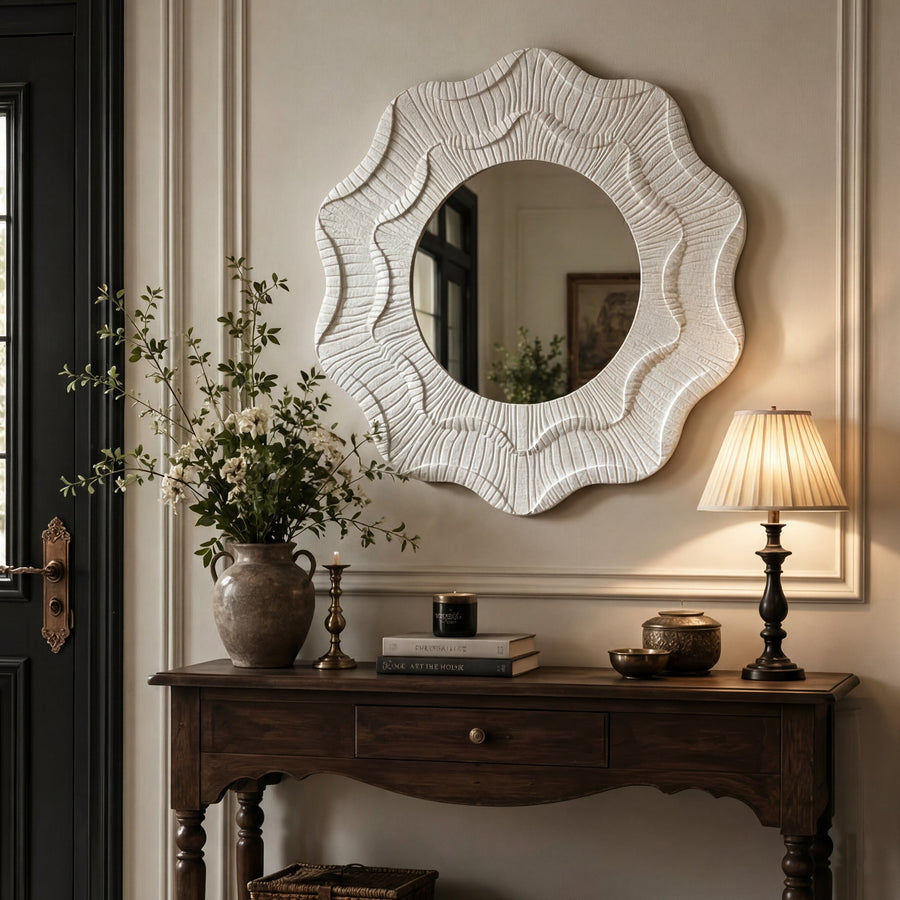 Wavy flower wall mirror above a dark wood console with a lamp and greenery