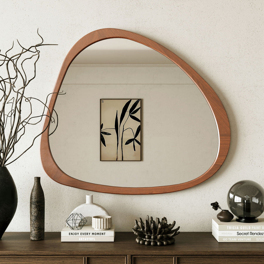 Asymmetrical wood wall mirror above a dark console styled with decor