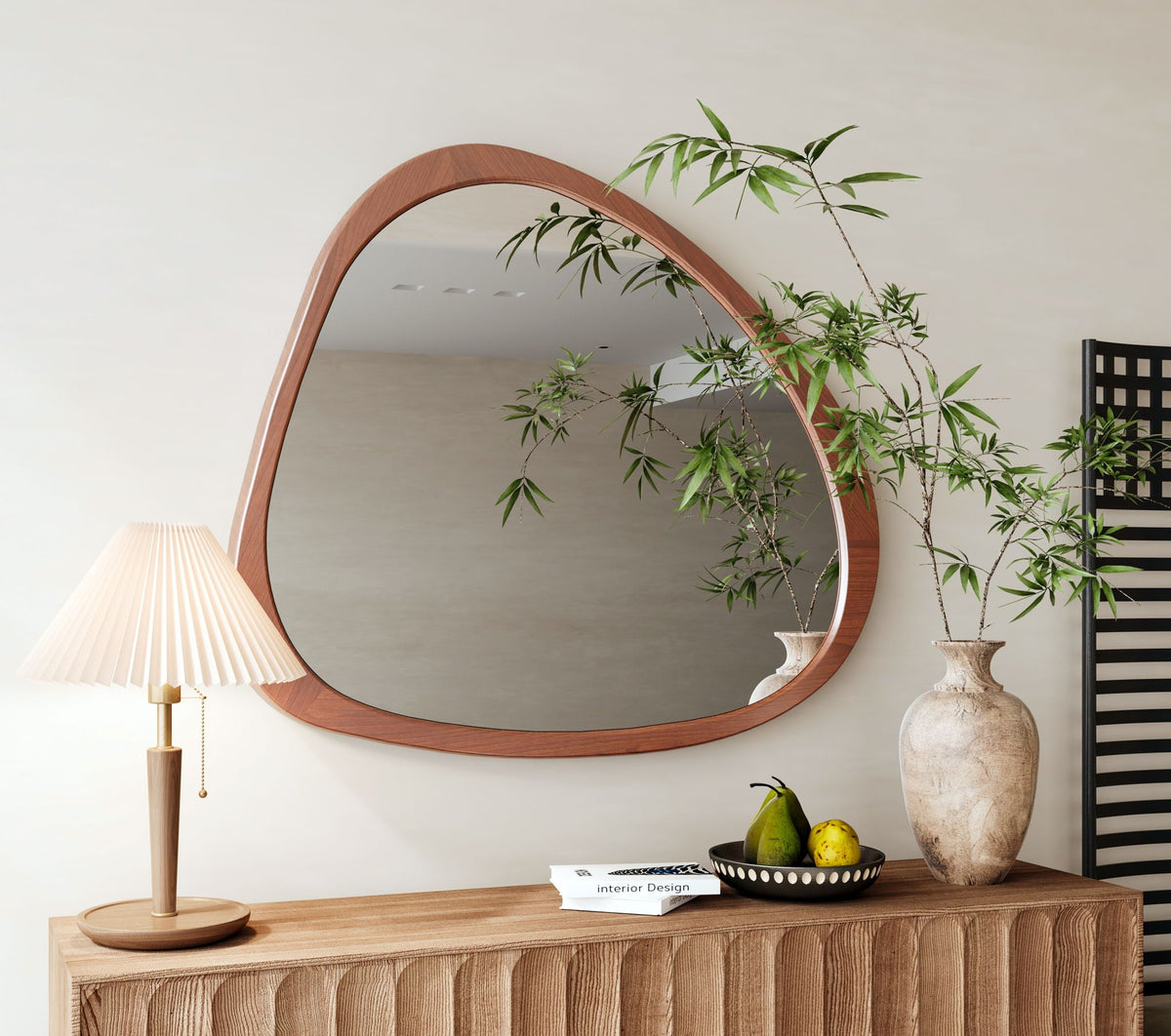 Asymmetrical wood wall mirror over a sideboard with a table lamp and greenery