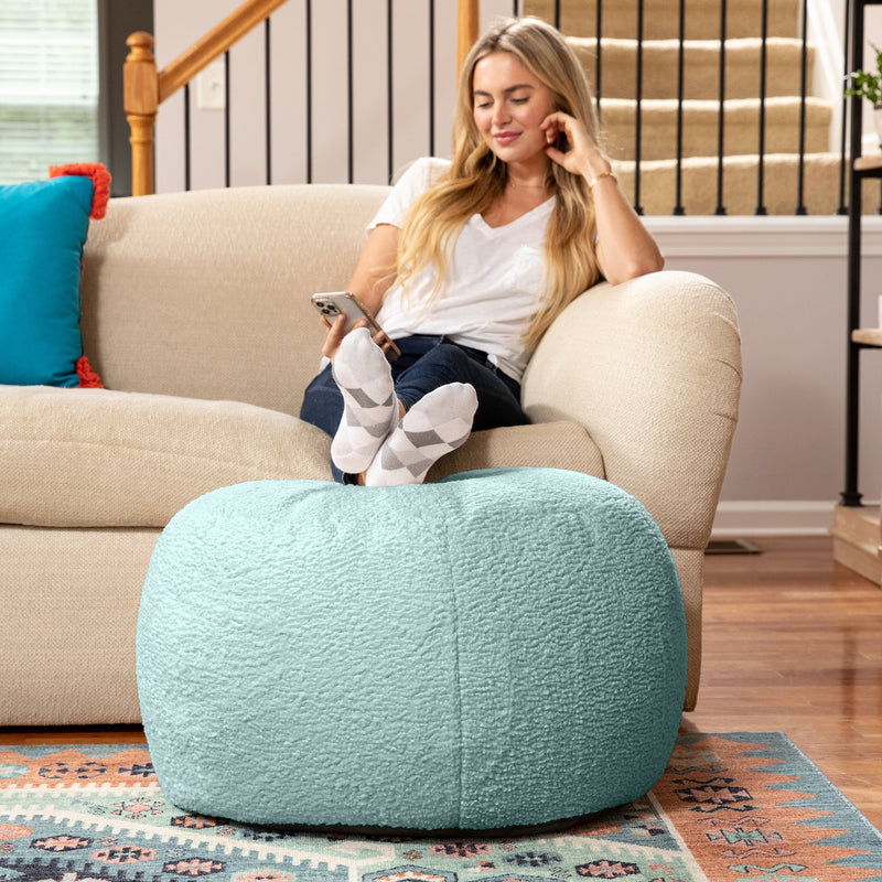 Woman sitting on a beige armchair with a blue ottoman in front of her, holding a phone.