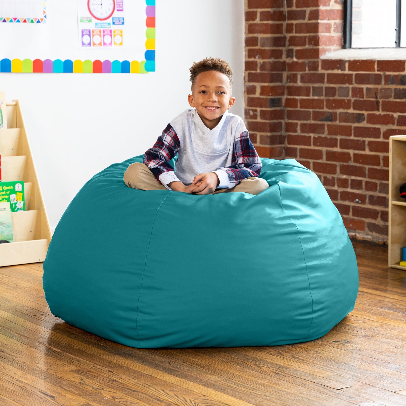 Child sitting on a teal bean bag chair in a room with a brick wall and colorful decorations.
