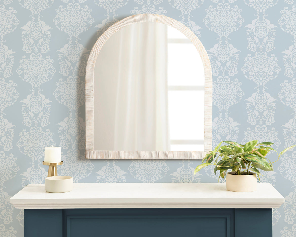 White rattan arch mirror above a console with a blue wall