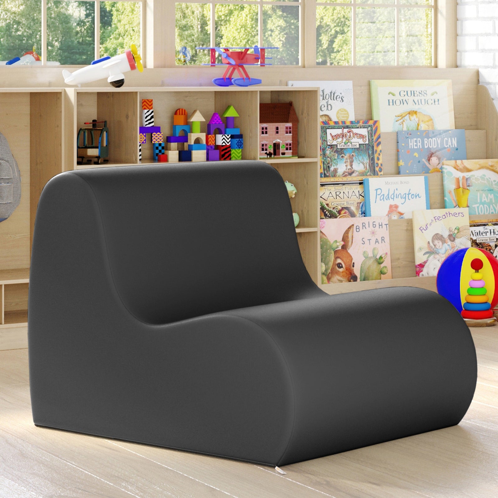 Children's reading nook with a dark gray upholstered chair, books, and toys in a bright room.