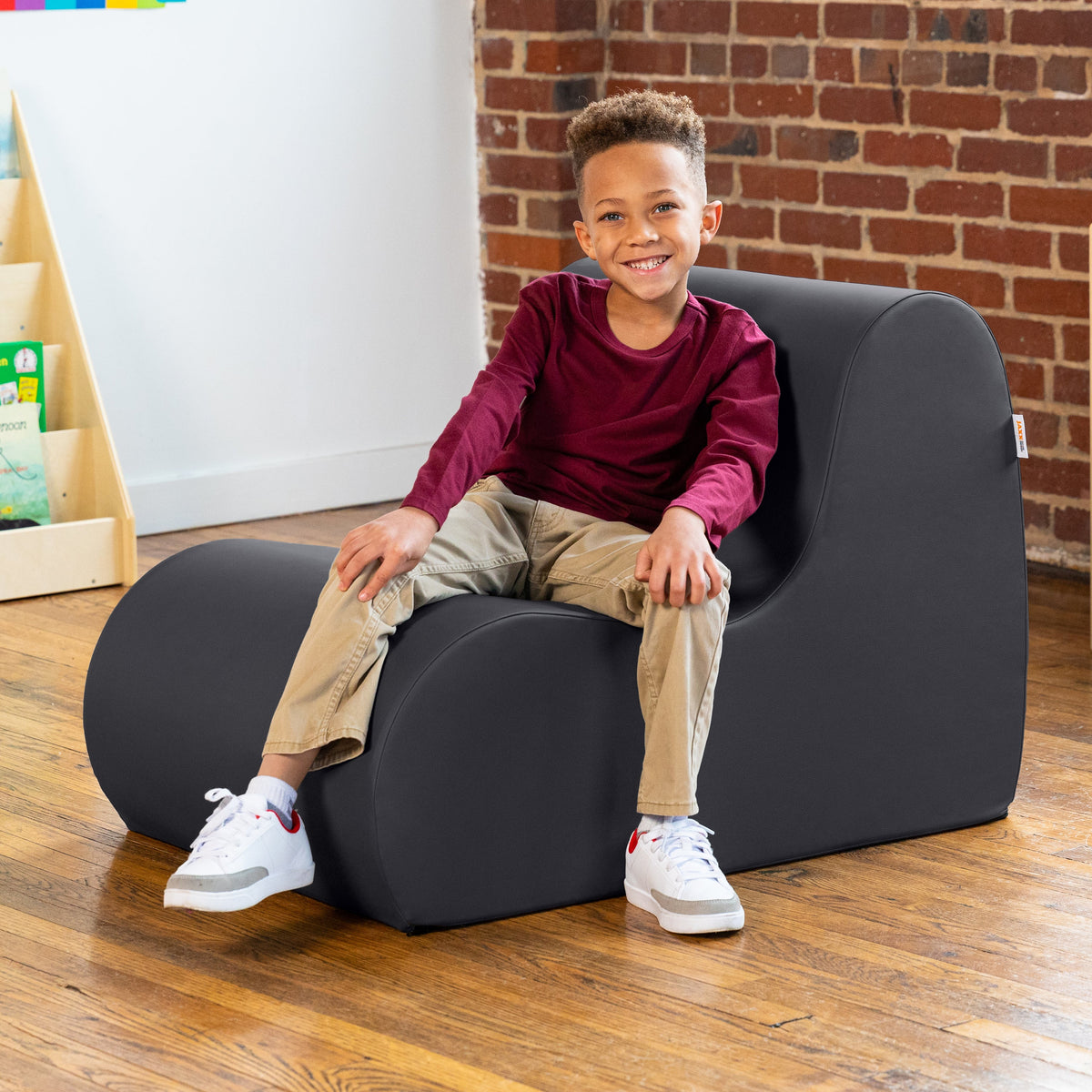 Child sitting on a black chair in a room with a brick wall and wooden floor.