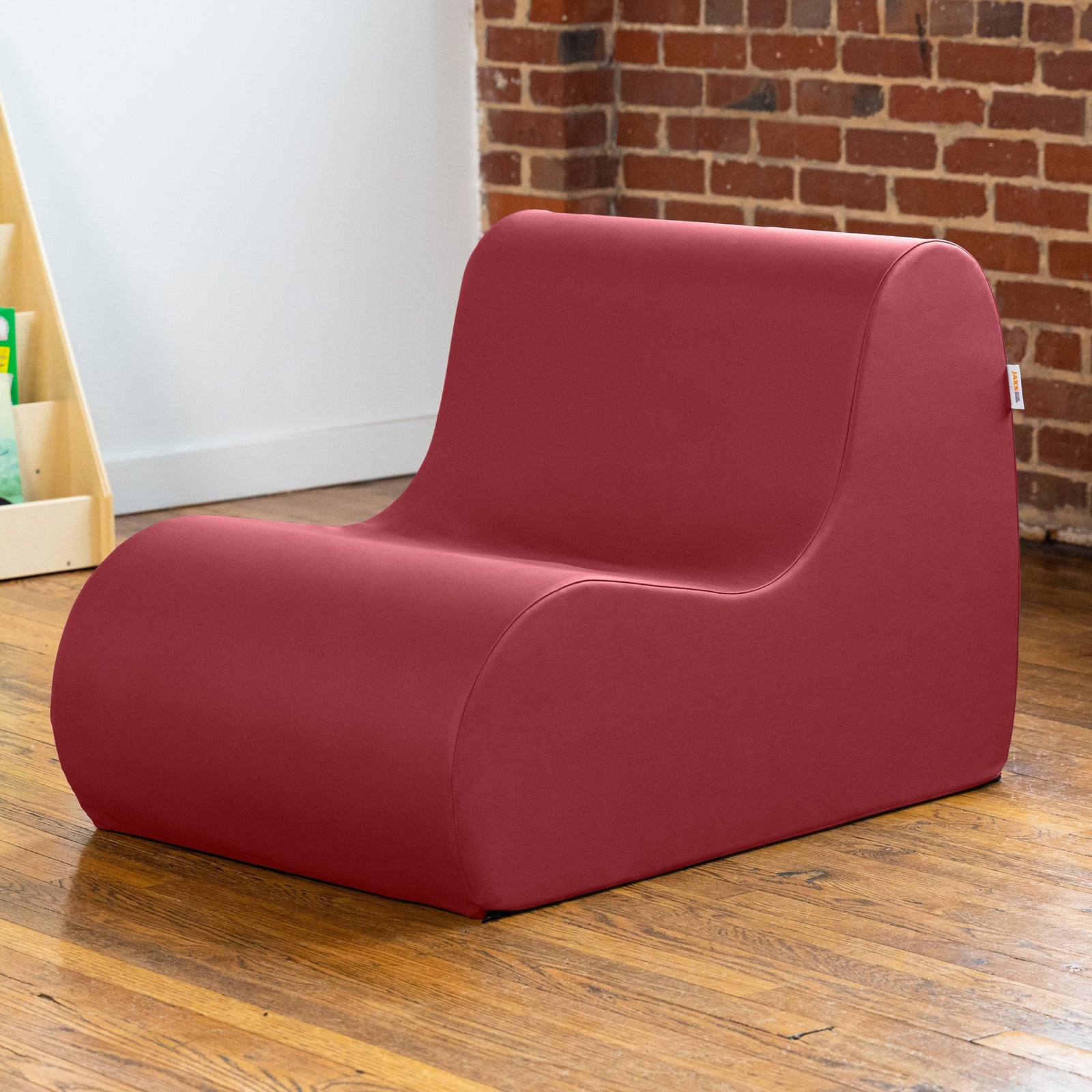 Red children's chair on a wooden floor with a brick wall in the background