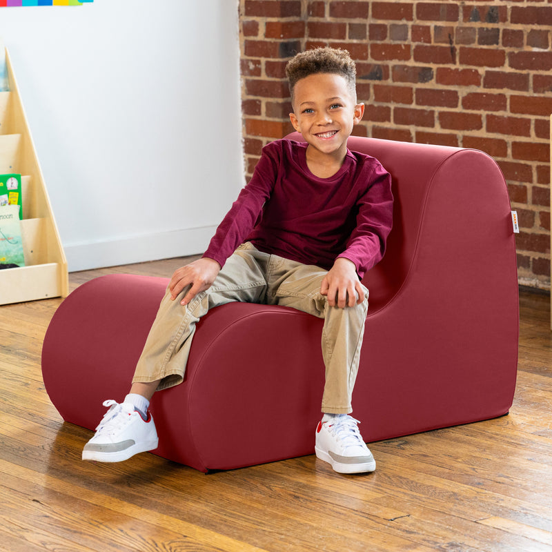 Child sitting on a red chair in a room with a brick wall and wooden floor.