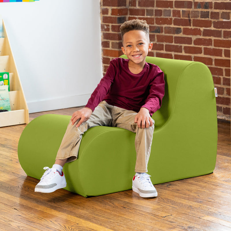 Child sitting on a green chair in a room with a brick wall and wooden floor.