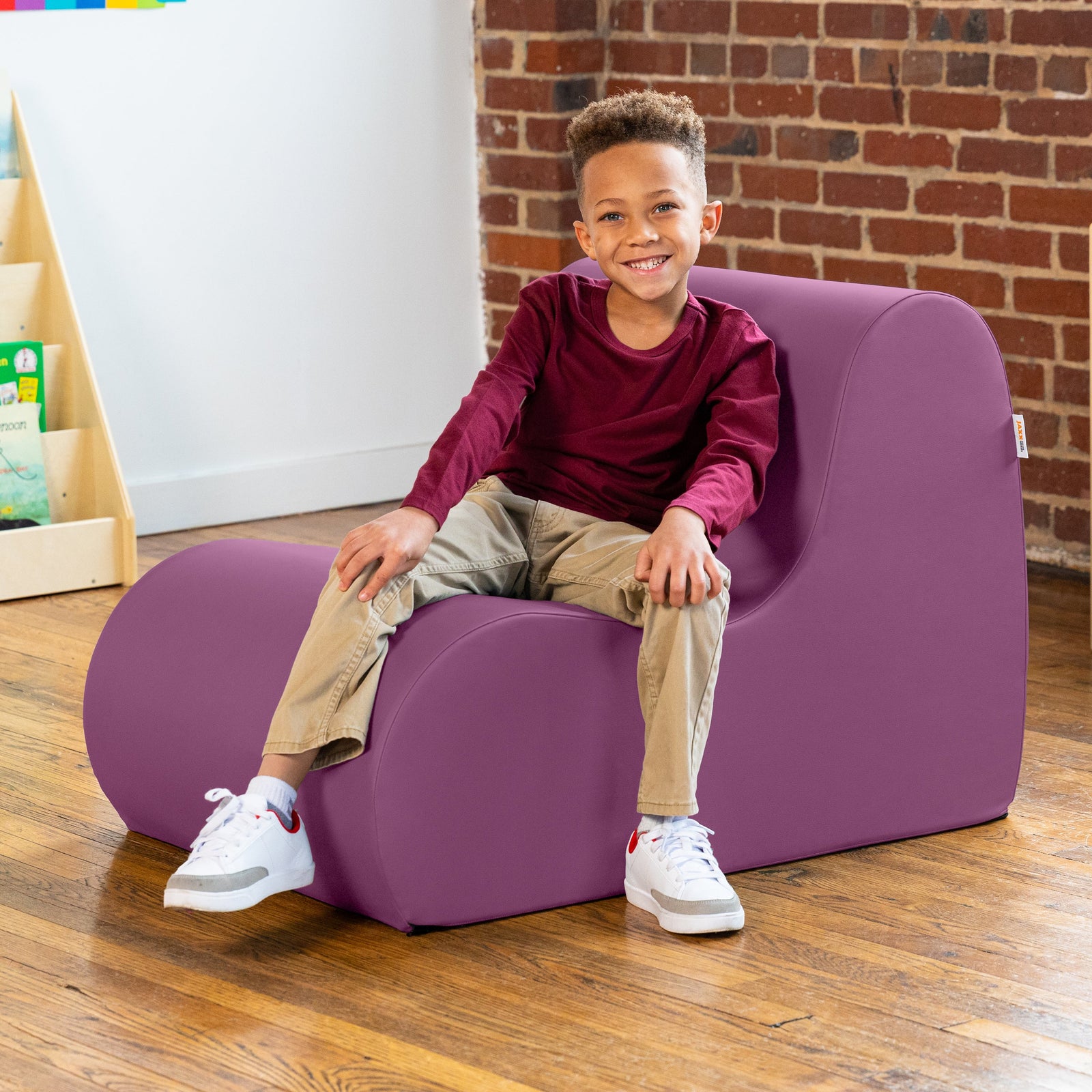Child sitting on a purple chair in a room with a brick wall and wooden floor.