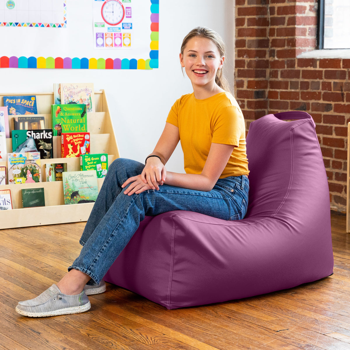 Woman sitting on a purple bean bag chair in a room with books and colorful decorations.