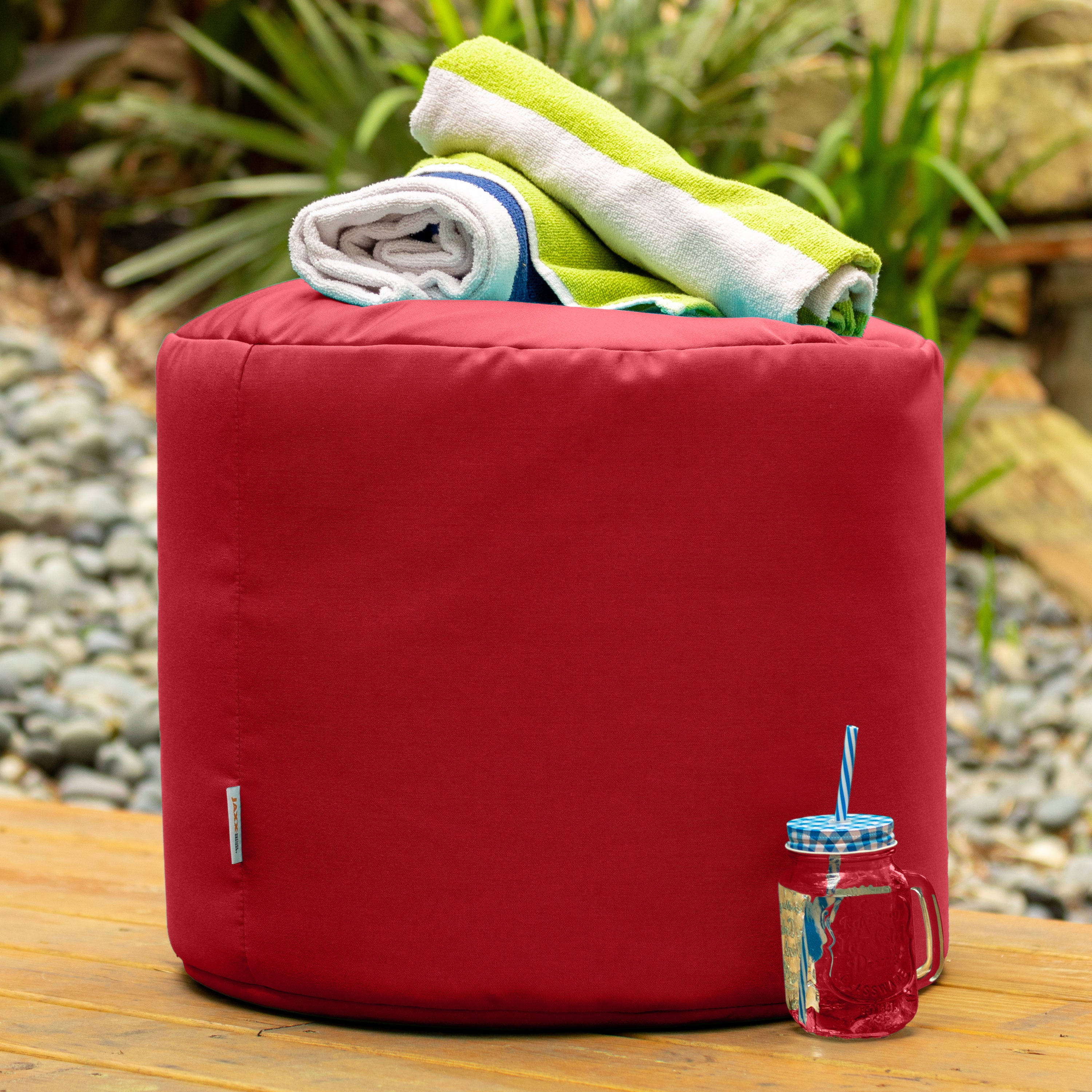 Red bean bag with folded towels on top, set against a natural outdoor background.